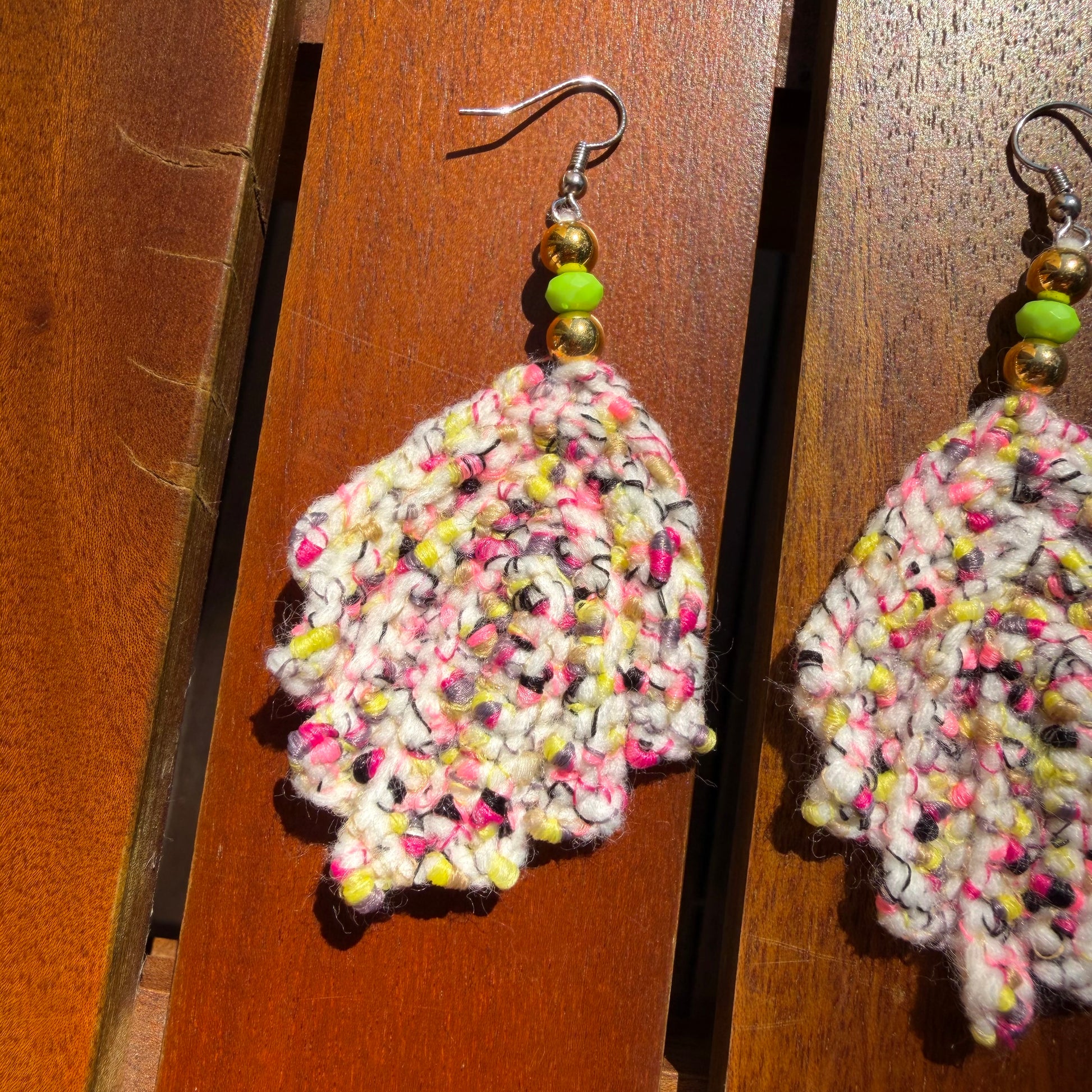 Colorful crocheted leaf-shaped earrings on a wooden surface