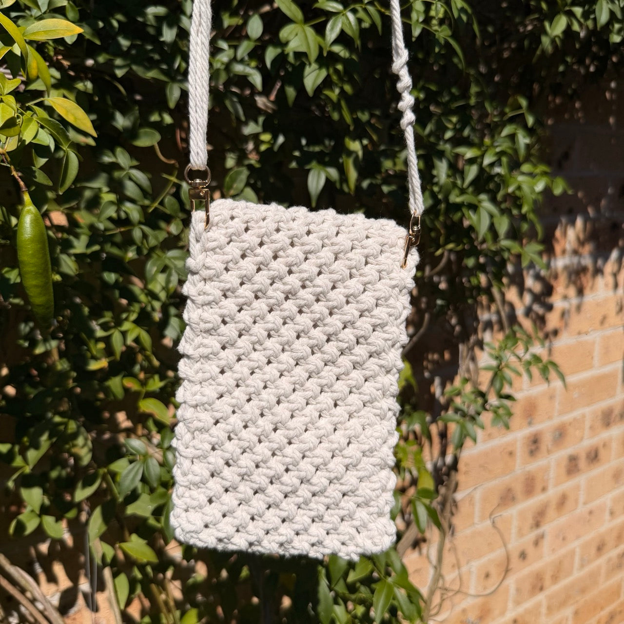 White woven handbag hanging from a tree branch with a brick wall in the background