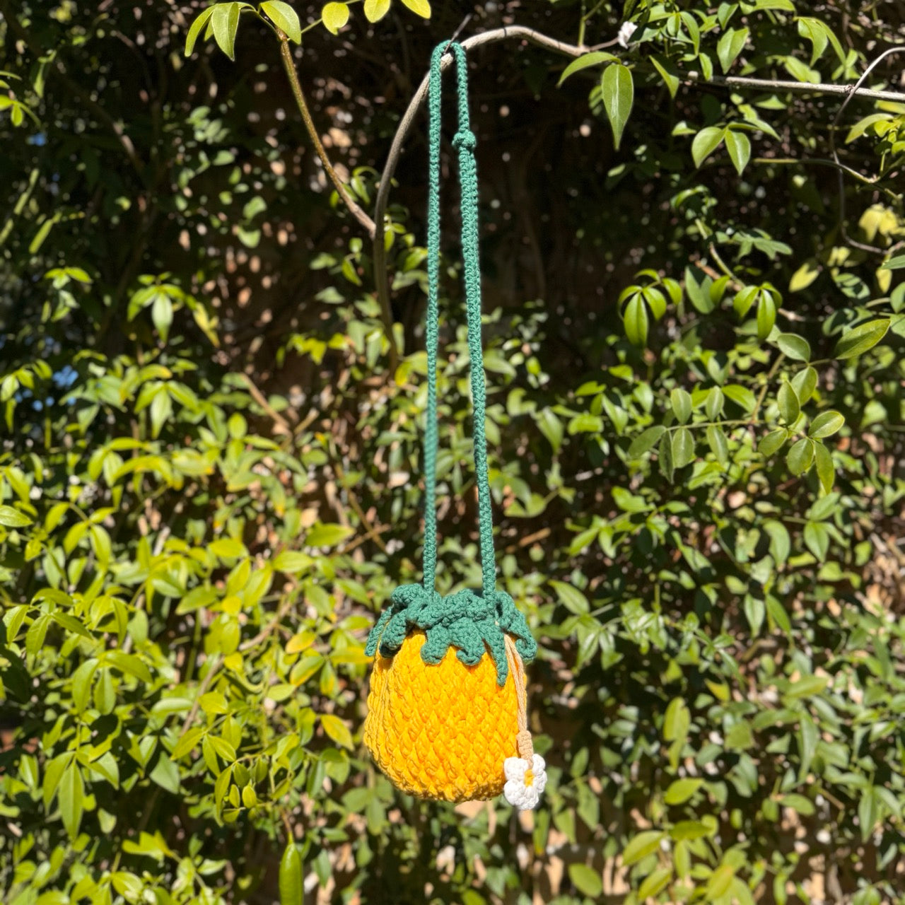 Handmade pineapple-shaped bag with green top hanging from a tree branch.